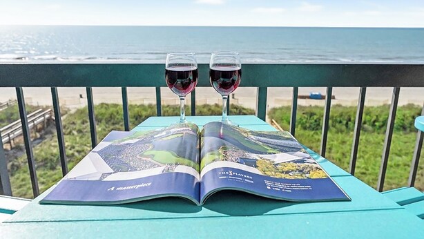 A brochure on a table with two glasses of red wine, overlooking a beach.