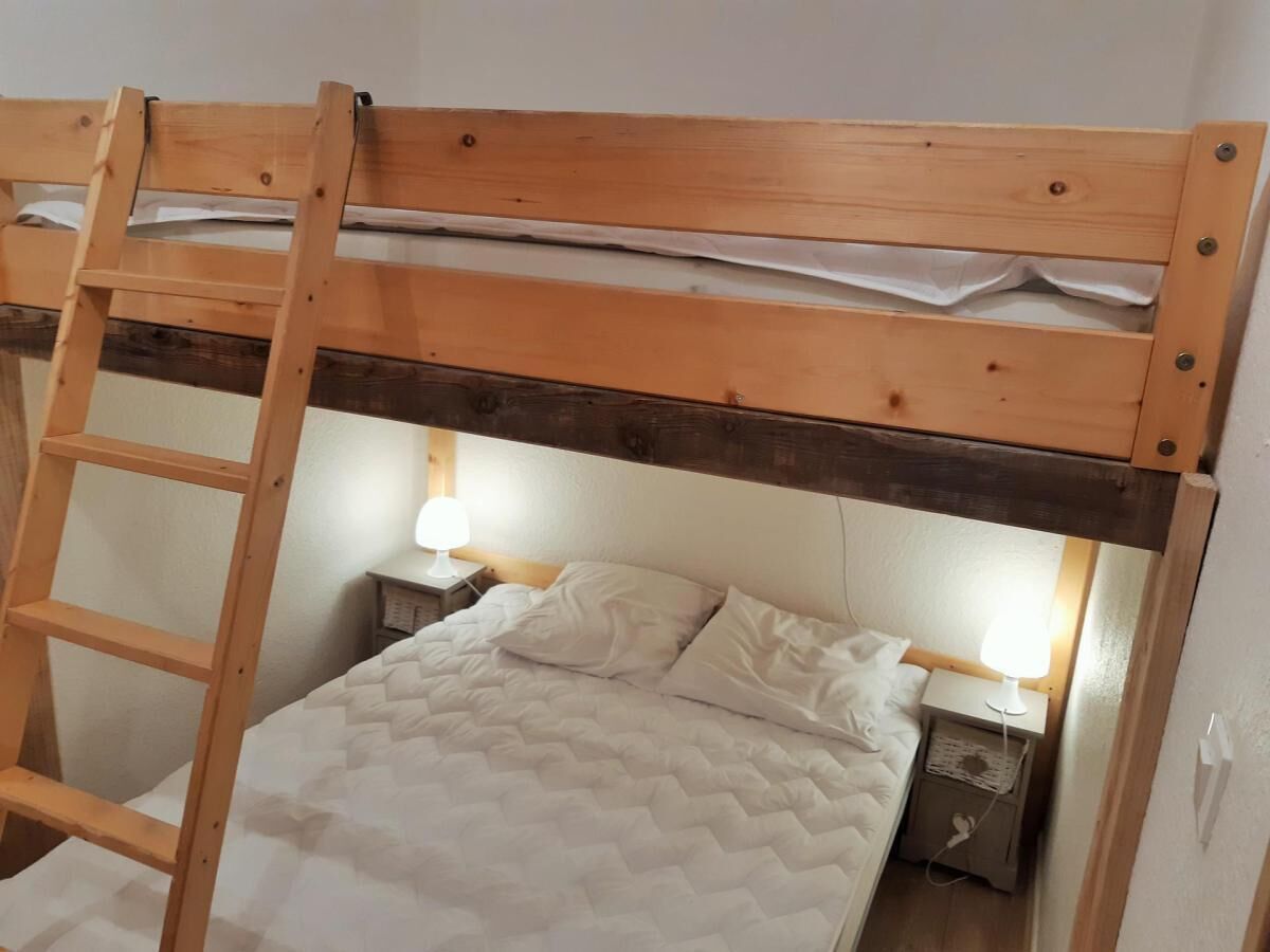 A bunk bed with a wooden ladder, two bedside tables with lamps, and a quilted bedspread.