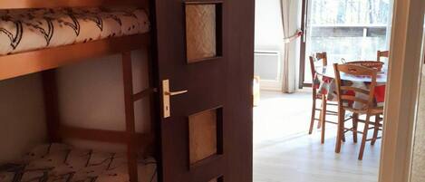 A room with a bunk bed, a door with a window, and a dining area with chairs and a table.