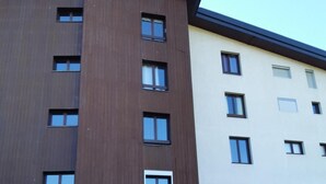 Ein mehrgeschossiges Gebäude mit moderner Architektur, das eine Kombination aus braunen und weißen Außenwänden, zahlreichen Fenstern und einem zentralen Eingang mit Glastür aufweist.