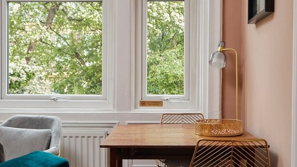 A room with a wooden table, two chairs, a gold lamp, and a window with a view of trees. - Scandi Chique Newcastle Abode (Newcastle upon Tyne)
