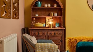 A cozy room with a wooden cabinet, a radiator, a bed with a patterned blanket, and a fluffy green pillow. - Scandi Chique Newcastle Abode (Newcastle upon Tyne)