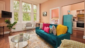 A living room with a teal sofa, a glass coffee table, a television, and a kitchen area with a teal refrigerator. - Scandi Chique Newcastle Abode (Newcastle upon Tyne)
