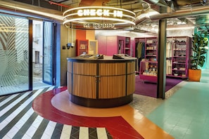 A check-in counter with a circular design, a glass door entrance, and a clothing store with shelves. - The Social Hub Madrid (Madrid)