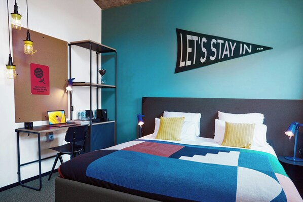 Una habitación de hotel con cama, escritorio, silla, estanterías y un cartel en la pared.