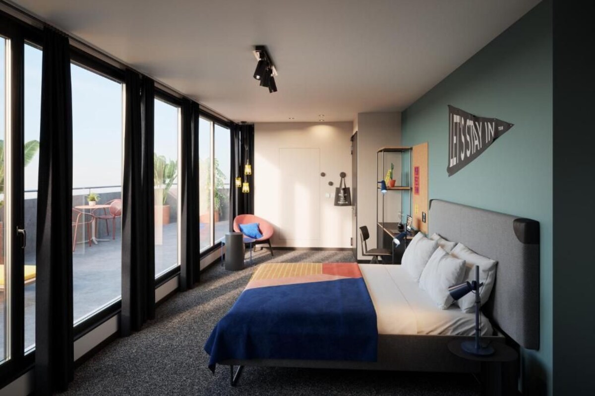 Habitación de hotel moderna con una cama grande, un escritorio y una silla. Cuenta con ventanas amplias y vistas al exterior.