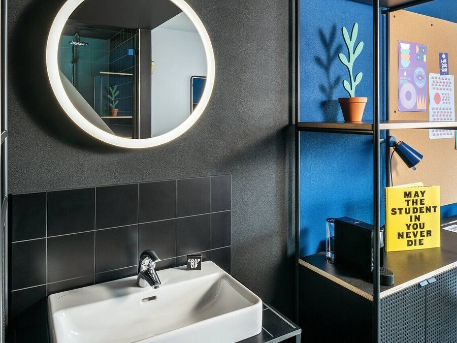 Un baño con un lavamanos blanco, un espejo redondo y una pared de azulejos negros.