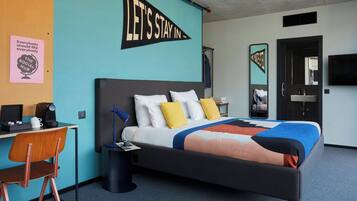 A hotel room with a bed, desk, chair, and a motivational poster on the wall.