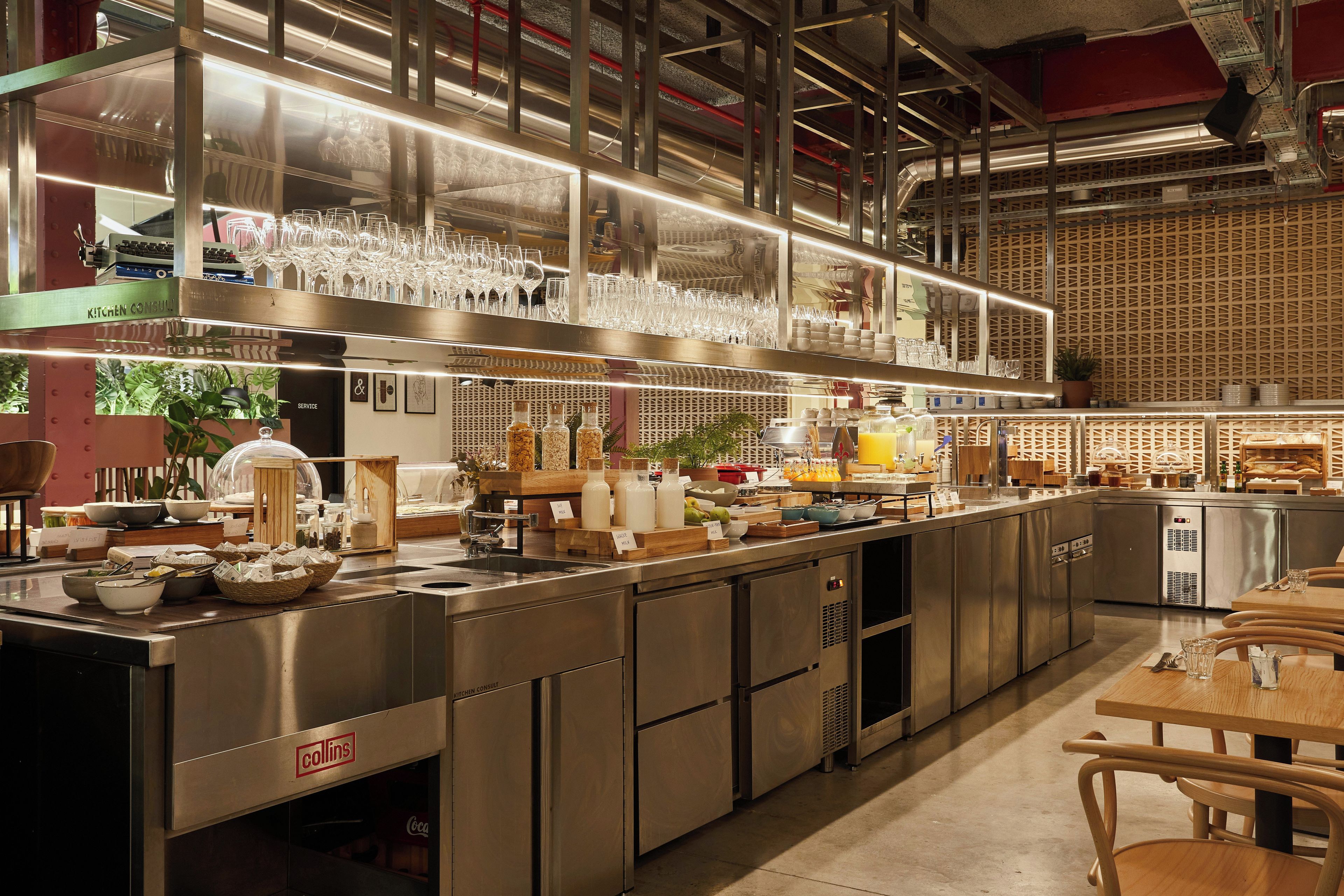 Cocina comercial con electrodomésticos de acero inoxidable, una barra de servicio y una zona de estar con mesas y sillas de madera.