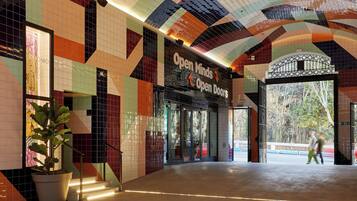 Ein modernes Gebäude mit farbenfrohen Mosaikfliesen, einem Schild mit der Aufschrift 'Open Minds Open Doors' und einem großen Glas Eingang.