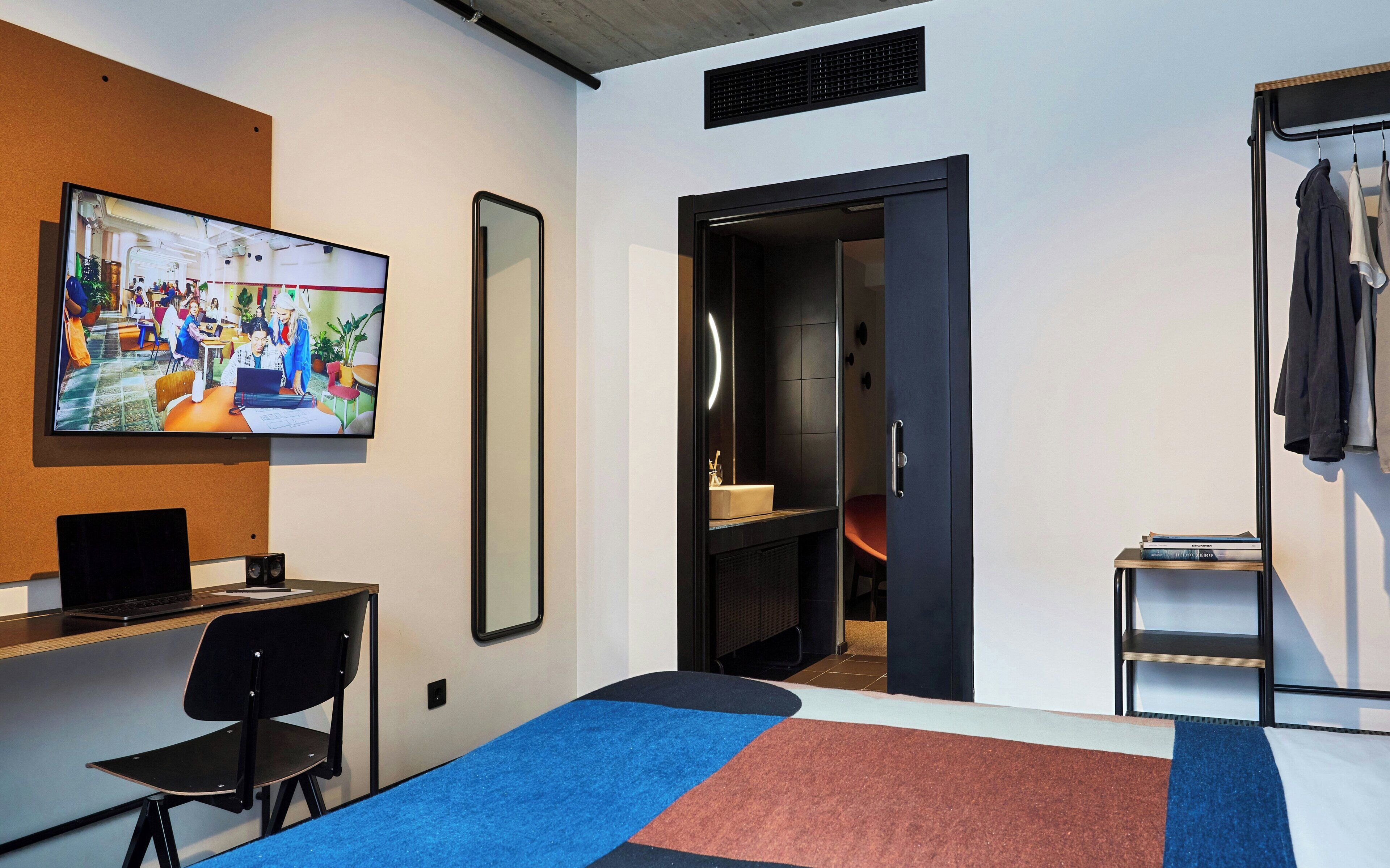 Una habitación de hotel moderna con escritorio, silla, televisor y puerta que da a un baño.