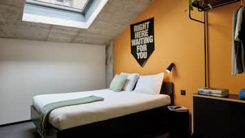 Una camera da letto con un letto, un comodino, una lampada, una pianta e un cartello appeso al muro.