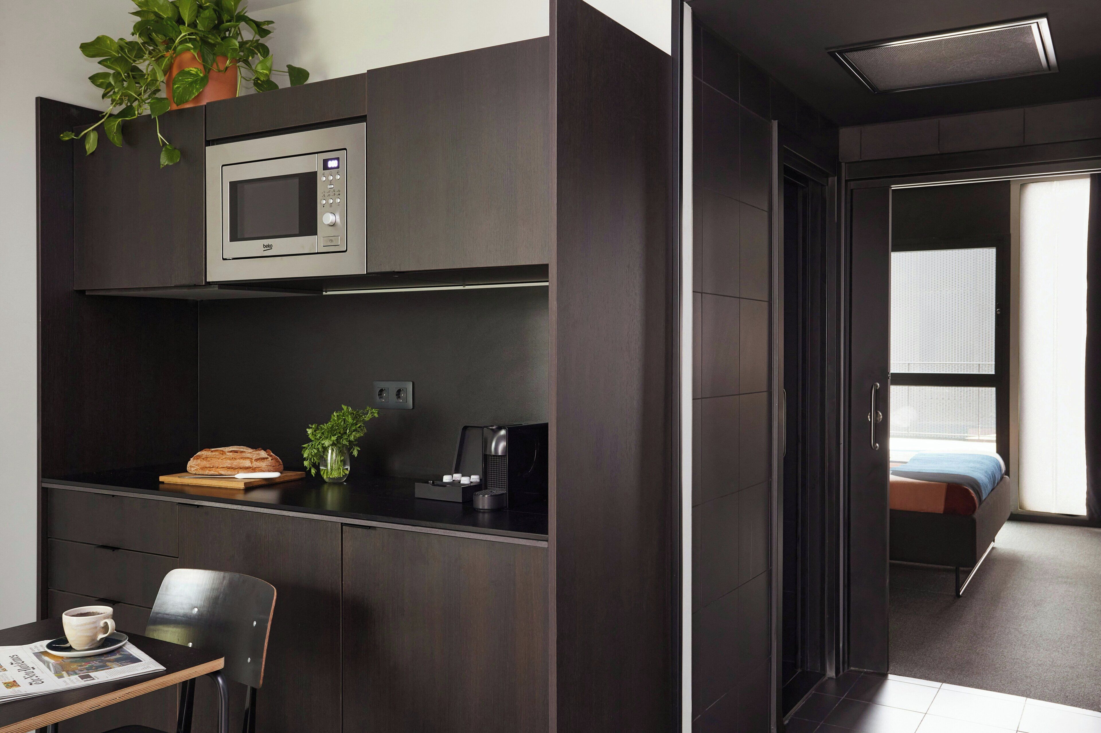 A modern kitchenette with a microwave, coffee machine, and a loaf of bread.