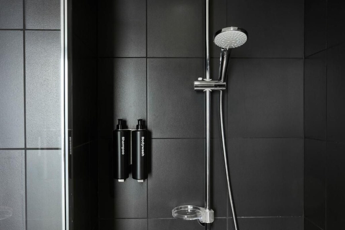 Um banheiro moderno com piso de azulejos pretos, um chuveiro e duas embalagens de hidratante corporal e shampoo.