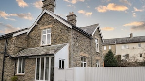 Une maison en pierre avec une porte blanche, un petit porche et une clôture blanche à l’avant.