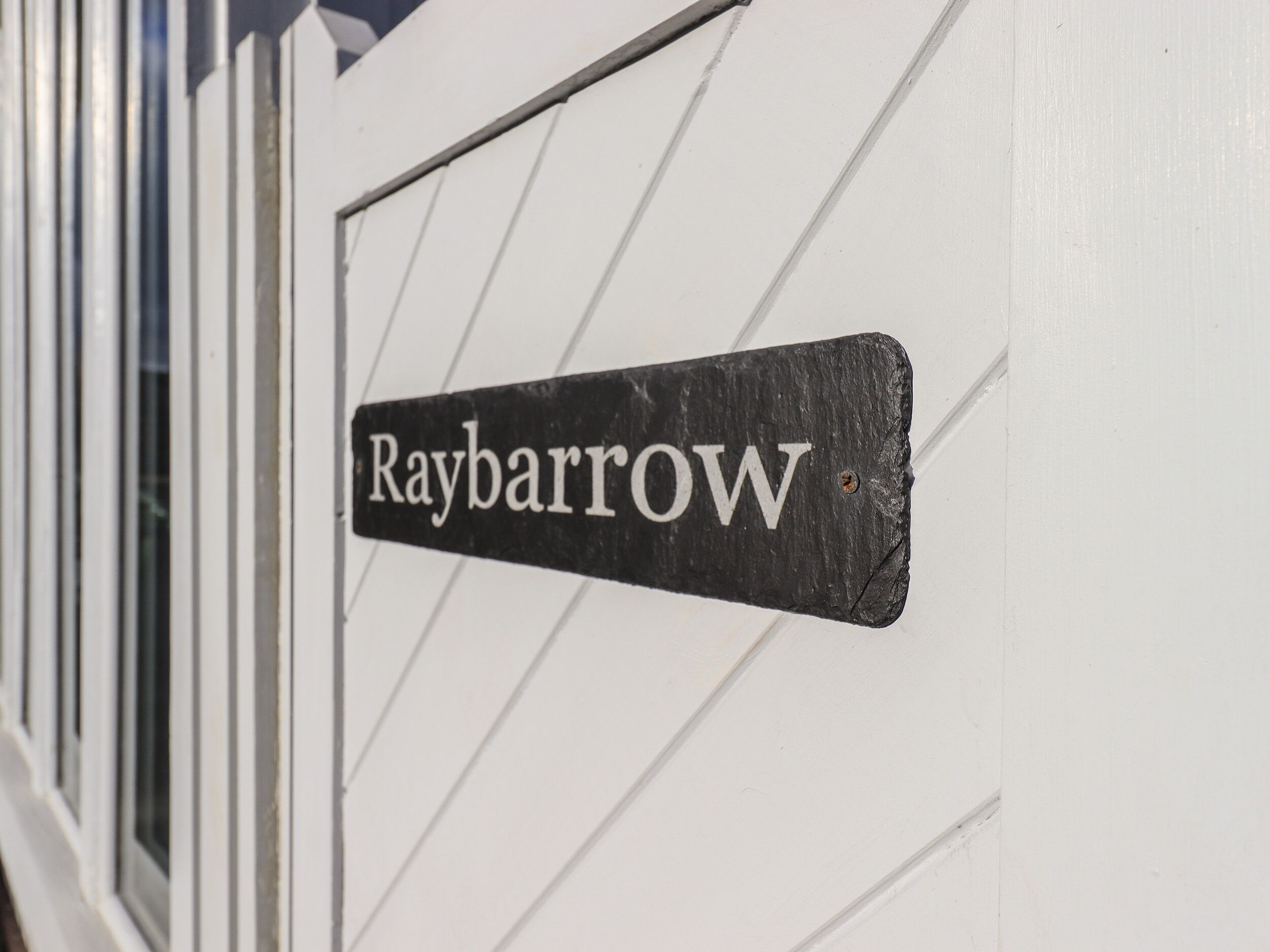 Ein schwarzes Metallschild mit dem Schriftzug "Raybarrow" an einer weißen Wand.