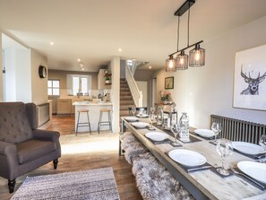 A modern kitchen with a central island, a dining area with a long table set for six, and a cozy seating area with a plush sofa and a furry rug.