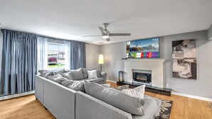 Una sala de estar moderna con un sofá modular, una chimenea, un ventilador de techo y un televisor montado en la pared.