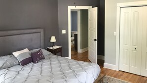 A bedroom with a bed, a nightstand, a ceiling fan, and a door leading to another room.