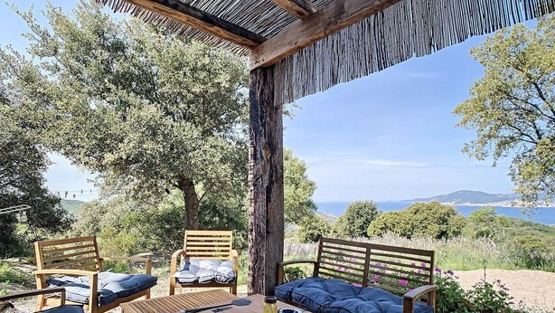 Un área de estar al aire libre con muebles de madera y una mesa, rodeada de árboles y vistas al paisaje.