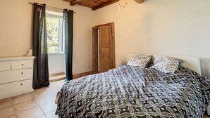 Un dormitorio con techo de madera, una cama con ropa de cama estampada, un aparador y una ventana con cortinas.