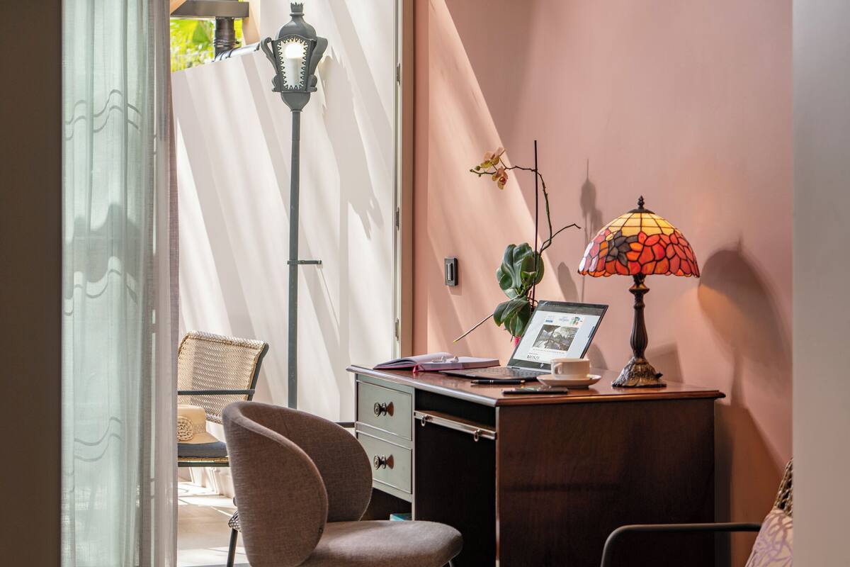 Quarto com escrivaninha, cadeira, abajur, laptop e um vaso de planta.