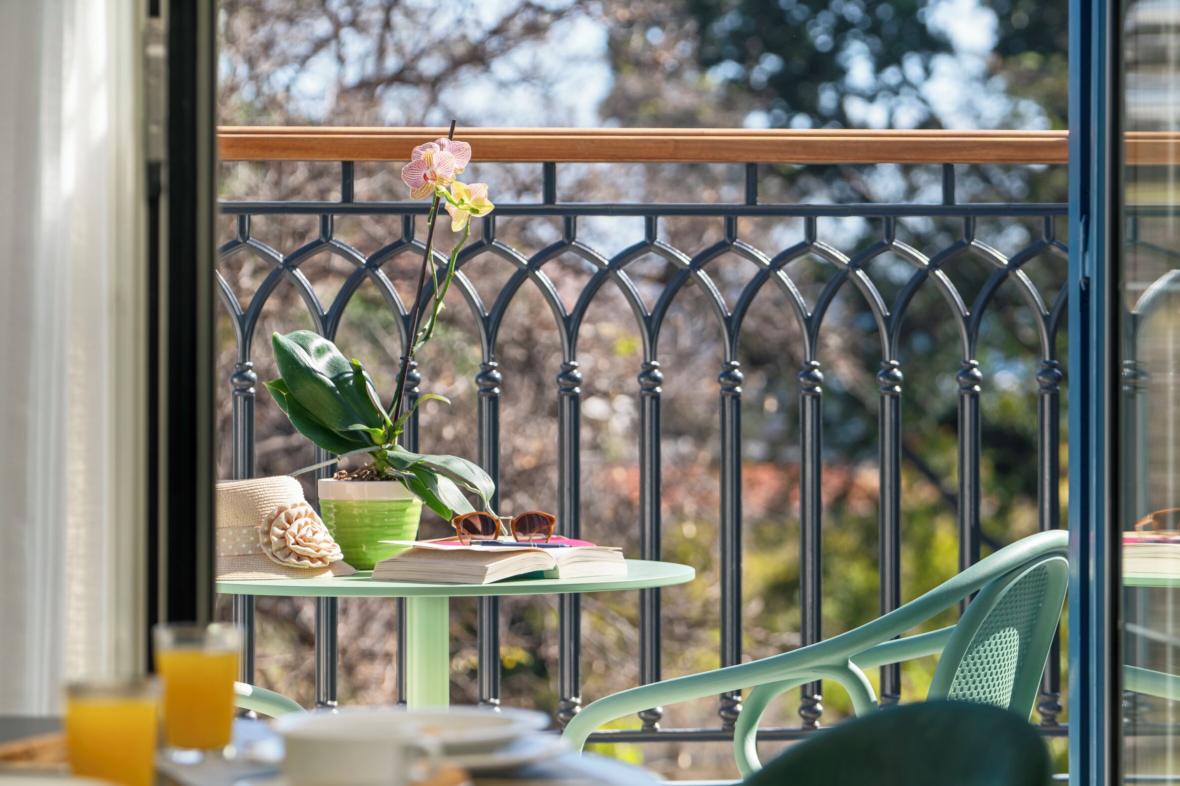 Un balcón con una mesa, una planta en maceta, un libro y un par de gafas de sol.