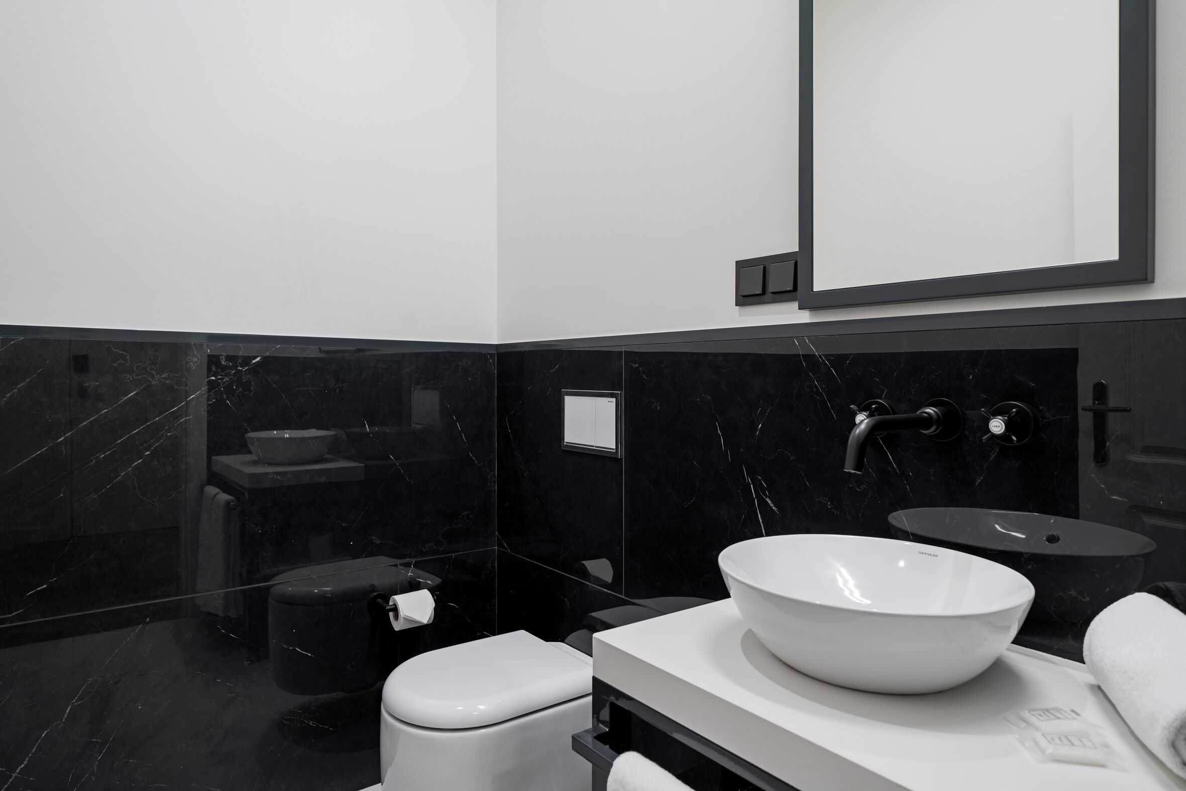 Ein modernes Badezimmer mit Toilette in Weiß, Waschbecken in Schwarz und einem großen Spiegel.