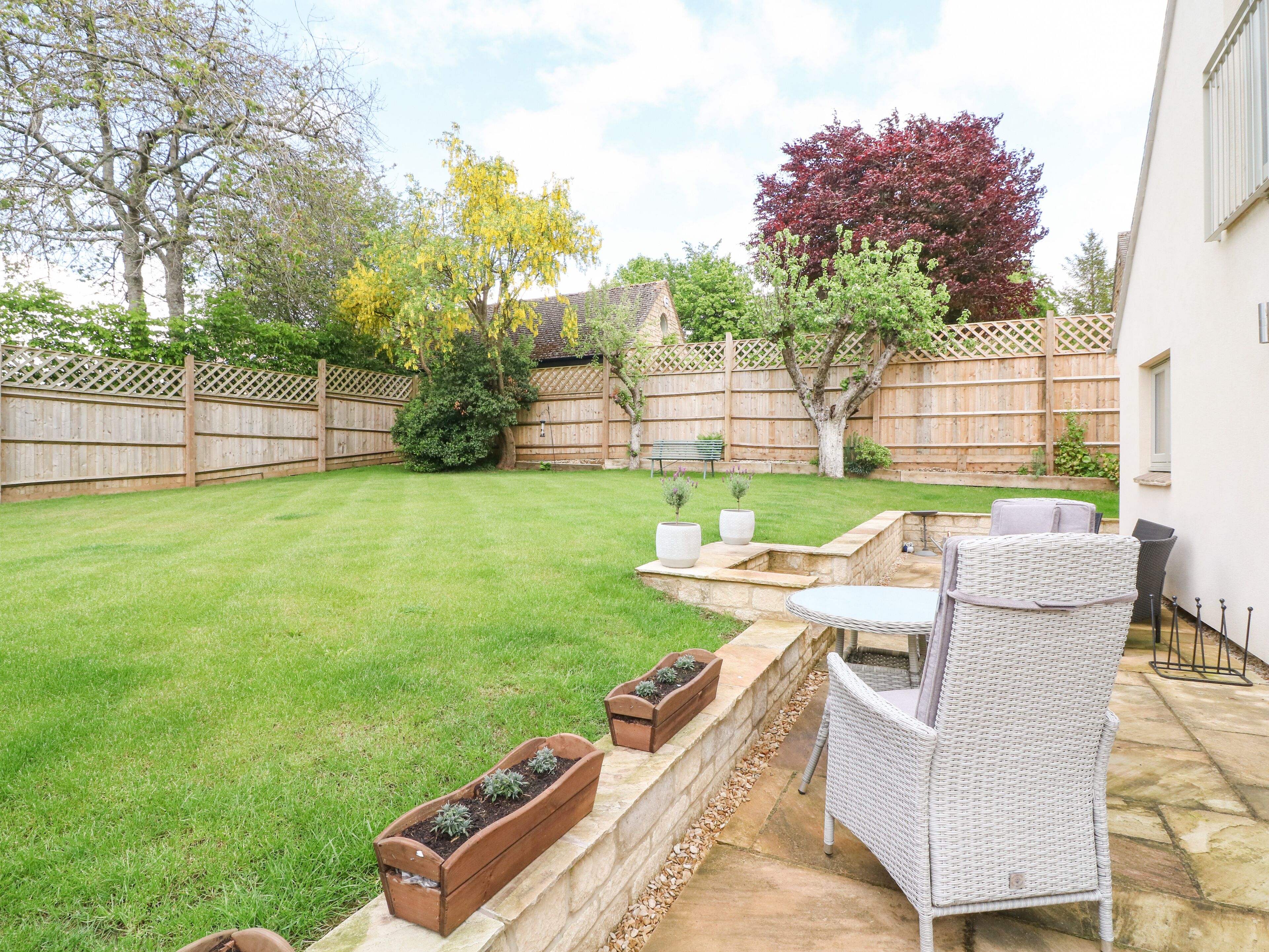 A backyard with a lawn, a wooden fence, a bench, and outdoor furniture.
