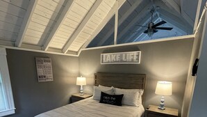 A bedroom with a large bed, two bedside tables with lamps, a ceiling fan, and a sign on the wall. - Cozy 3 bedroom seasonal cottage with very short walk to private community beach (Windham)