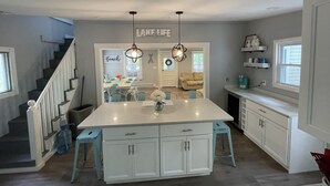 A modern kitchen with white cabinetry, a large island, and pendant lighting. - Cozy 3 bedroom seasonal cottage with very short walk to private community beach (Windham)