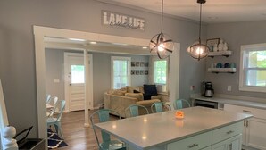 A modern kitchen with a central island, light-colored cabinets, and teal chairs. A sign above reads "LAKE LIFE." - Cozy 3 bedroom seasonal cottage with very short walk to private community beach (Windham)