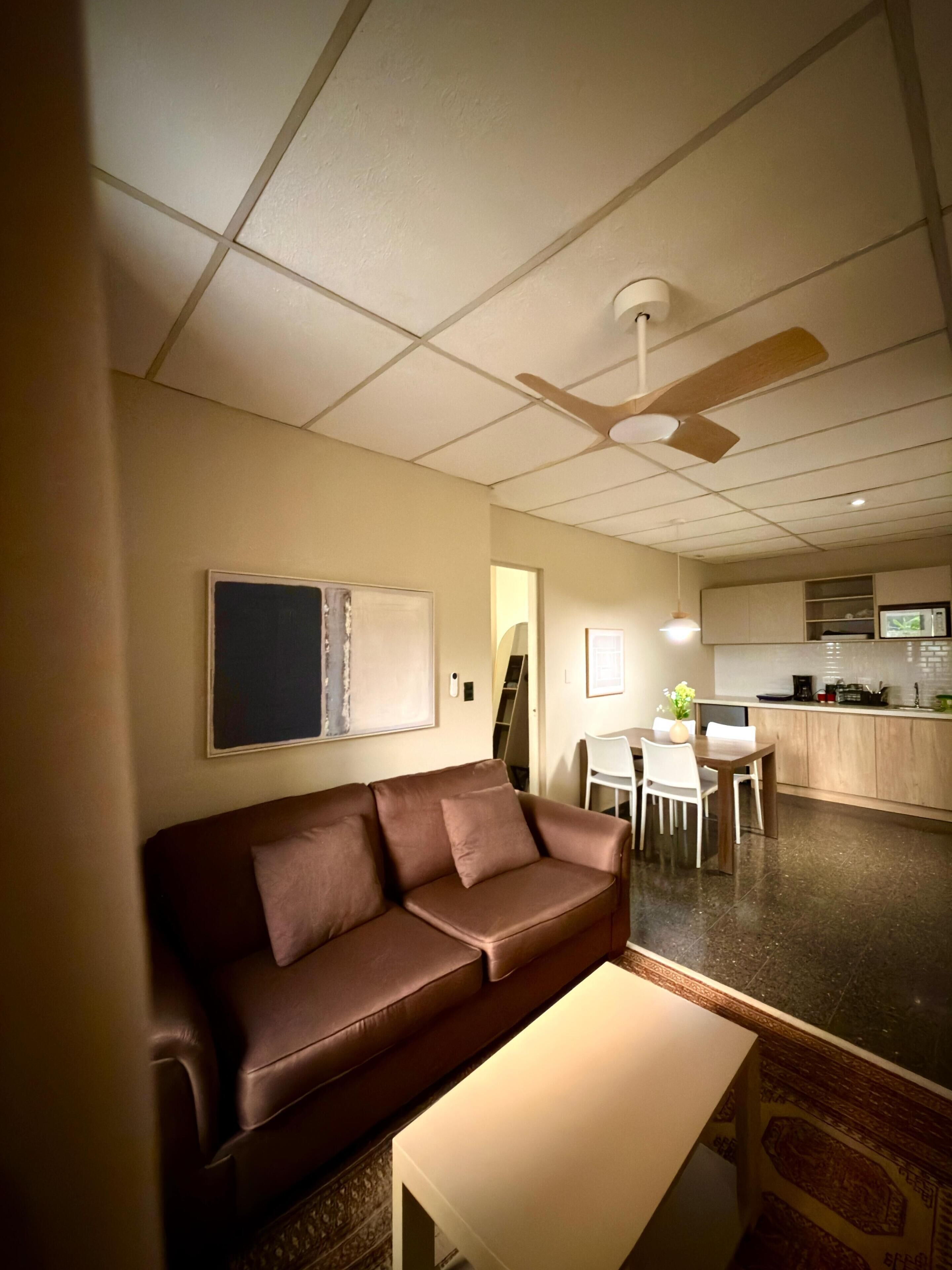 A living room with a brown sofa, a white table, and a ceiling fan.