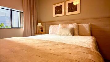 A hotel room with a large bed, a window with curtains, a nightstand with a lamp, and two framed pictures on the wall.