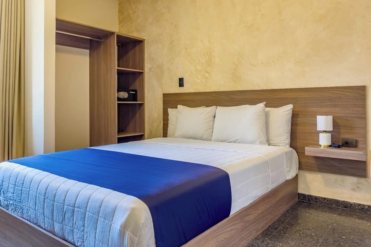 A hotel room with a bed, a wardrobe, and a bedside table with a lamp.