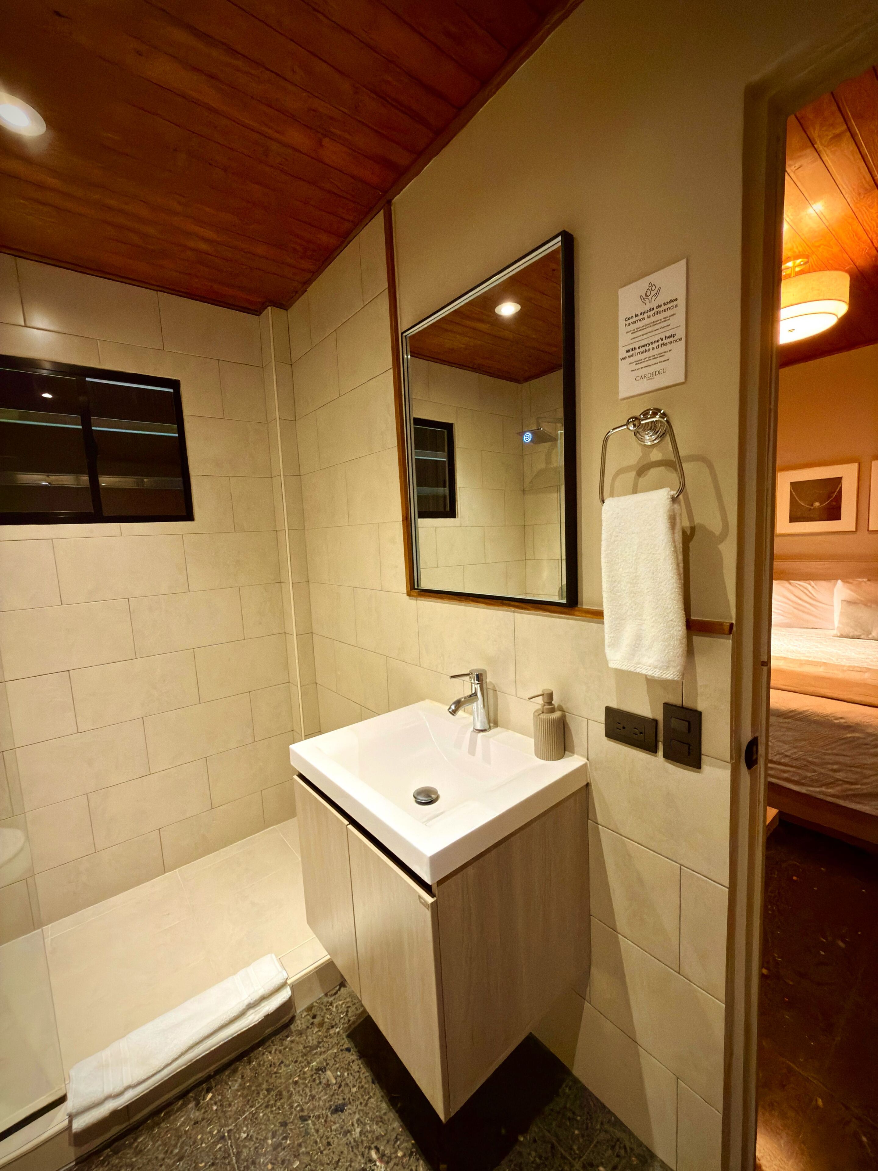 Un baño con lavamanos, espejo, toallero y ducha.