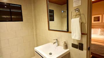 Un baño con lavamanos, espejo, toallero y ducha.