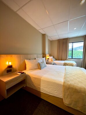 A hotel room with a large bed, bedside tables, a nightstand, a lamp, and a window with curtains. - Cardedeu San Benito Suites (San Salvador)