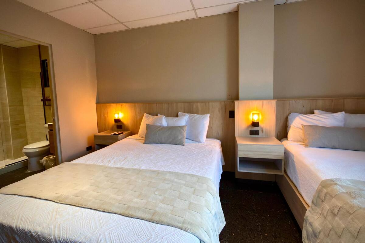A hotel room with two beds, a shower, and a toilet.