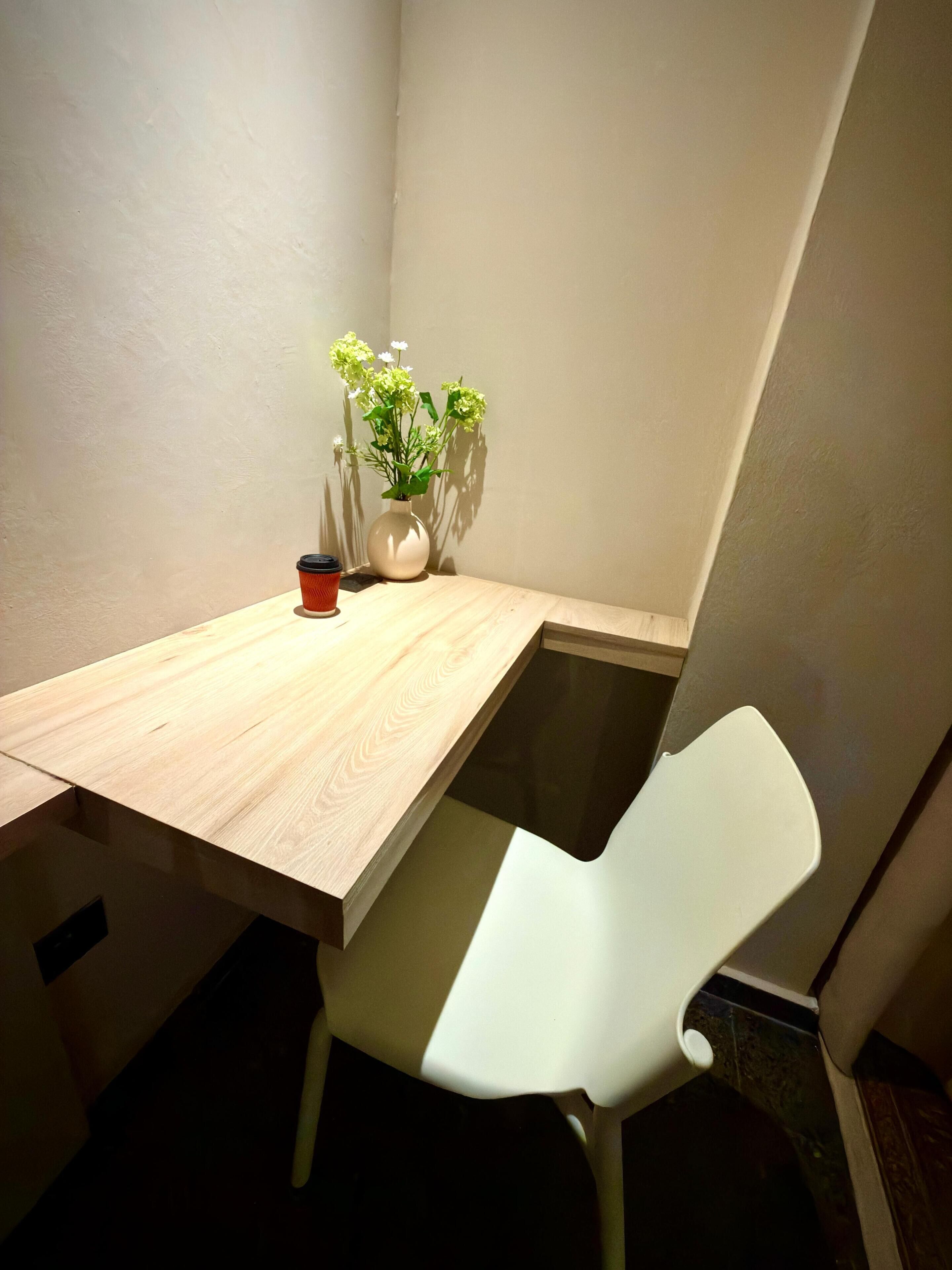 A corner room with a wooden table, a white chair, and a vase with flowers.
