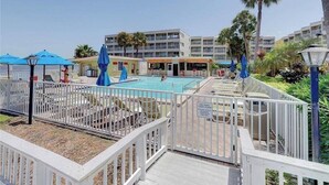 A pool area with lounge chairs and umbrellas, surrounded by a white fence. - Tiki Themed Condo on Tampa Bay (Tampa)