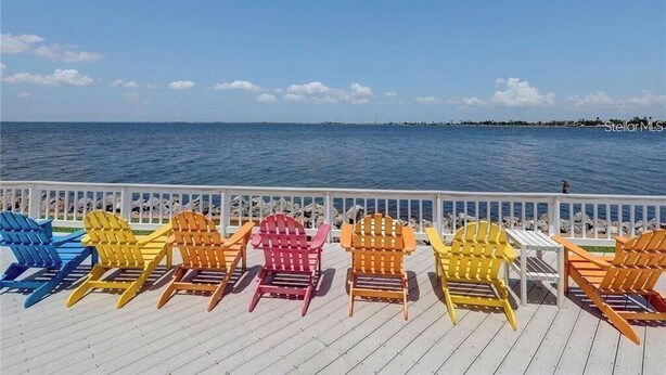 A deck with colorful Adirondack chairs facing a body of water. - Tiki Themed Condo on Tampa Bay (Tampa)