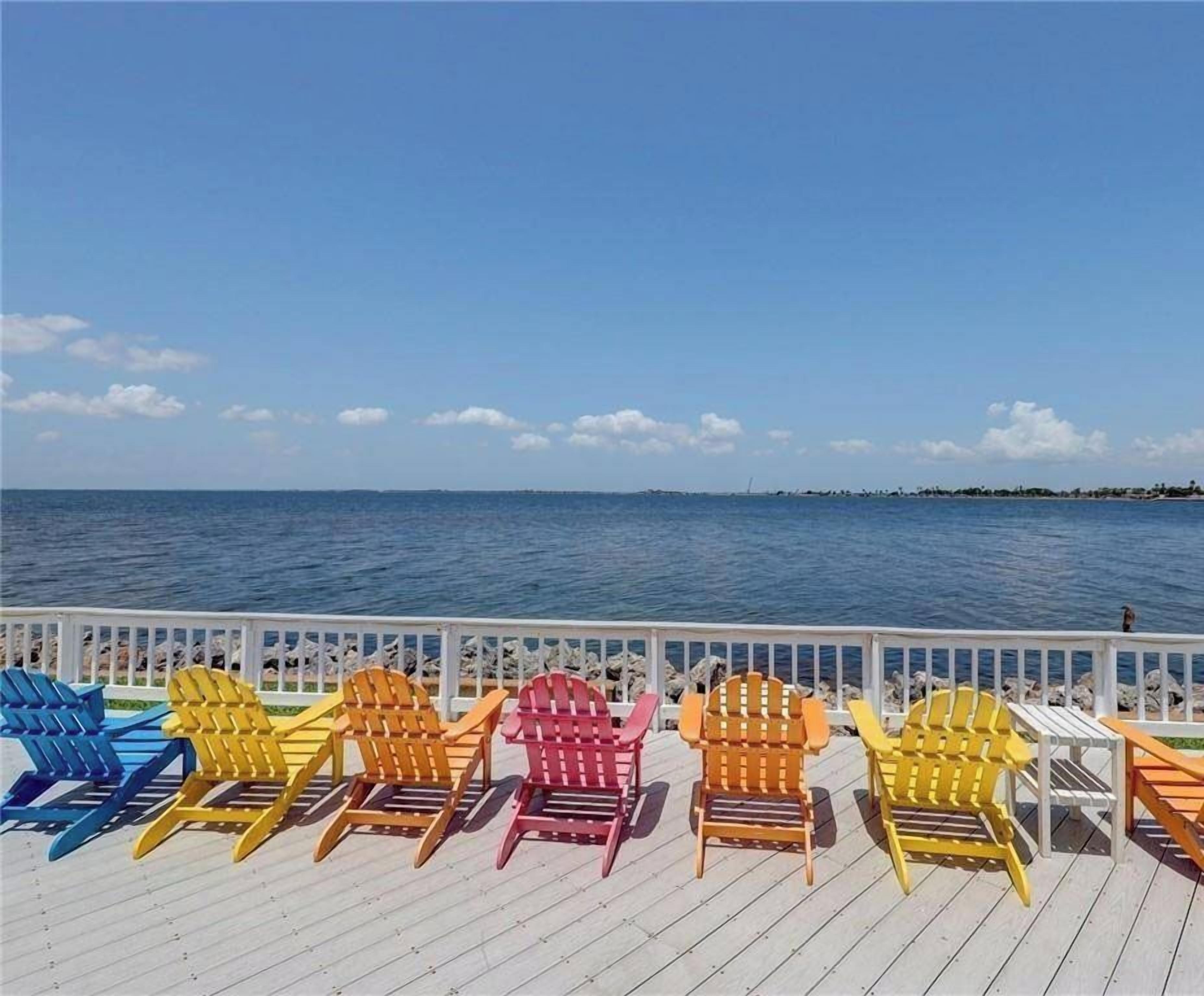Una terraza con sillas Adirondack de colores que dan a un cuerpo de agua.