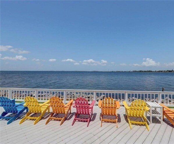A deck with colorful Adirondack chairs facing a body of water.