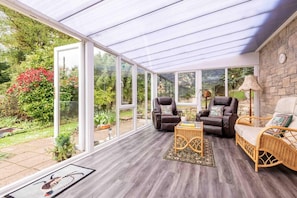 A conservatory with a glass ceiling, wicker furniture, and a view of a garden.