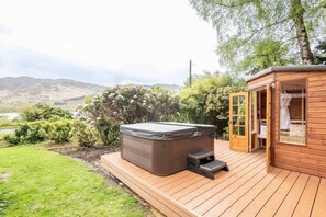 A hot tub on a wooden deck with a view of hills and a lake.