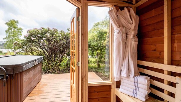 A wooden cabin with a hot tub, a bench, and a window overlooking a garden. - 3 Bedroom Bungalow With Htub & Private Loch Access (Crieff)