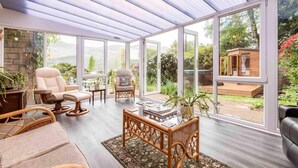 A sunroom with large windows, wicker furniture, and a view of a garden and outdoor hot tub. - 3 Bedroom Bungalow With Htub & Private Loch Access (Crieff)