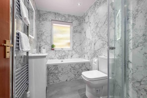 A bathroom with a marble backsplash, a window, a toilet, and a glass shower enclosure.