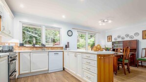A modern kitchen with white cabinetry, a wooden island, and a dining area with a wooden table and chairs. - 3 Bedroom Bungalow With Htub & Private Loch Access (Crieff)